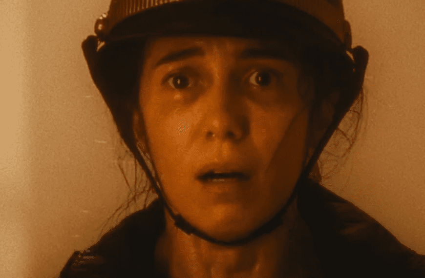 Marjorie Estiano, mulher branca com chapéu de bombeiro, olhando assustada em direção à câmera